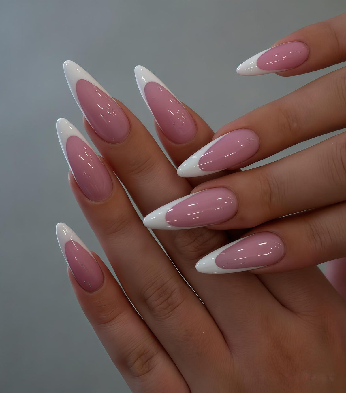 Close-up of a hand with long, almond-shaped nails. The nails feature a classic French manicure design, with a pale pink base and crisp white tips. The nails are glossy and well-manicured.