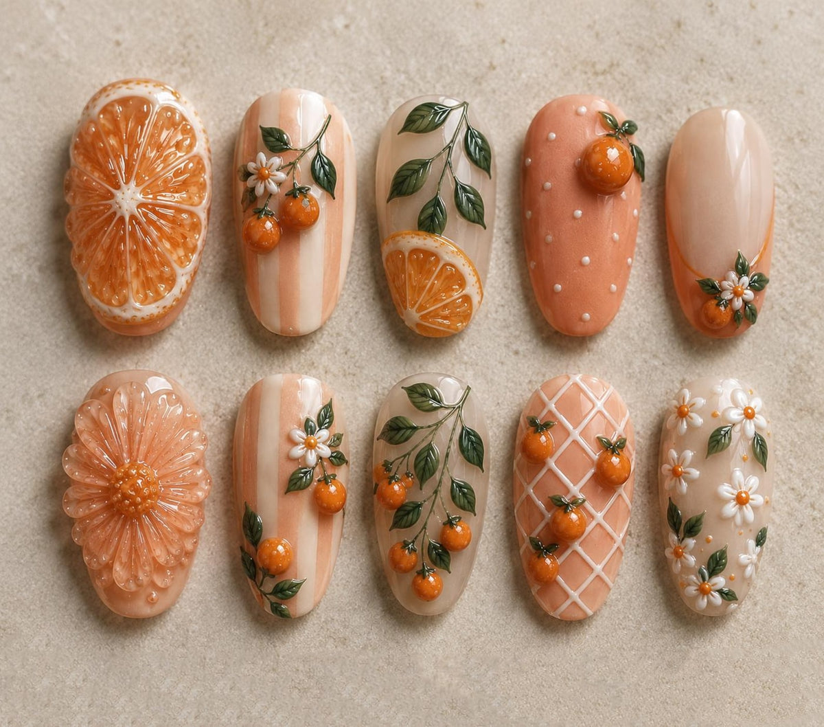 A collection of ten intricately designed nail art samples. The designs feature orange slices, flowers, and miniature oranges, with a color palette of orange, white, and peach. The nails showcase various textures and patterns.