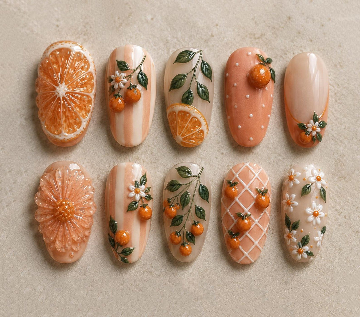 A collection of ten intricately designed nail art pieces. The designs feature orange slices, oranges, flowers, and leaves in shades of orange, white, and green. Some nails have a textured appearance, while others have a smooth, glossy finish.
