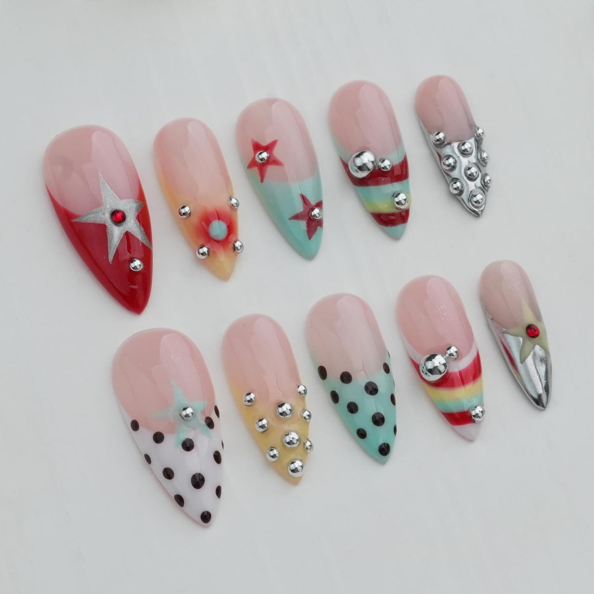 A collection of ten artificial nails with various designs. The nails feature a range of colors, including red, pink, and teal, and are adorned with stars, polka dots, and silver embellishments. Some nails have a French tip design.