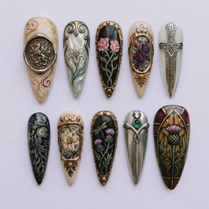 A collection of ten intricately designed nail art pieces. Each nail features unique artwork, including floral patterns, a griffin seal, and a dagger design. The color palette includes cream, gold, silver, black, and various shades of green and purple