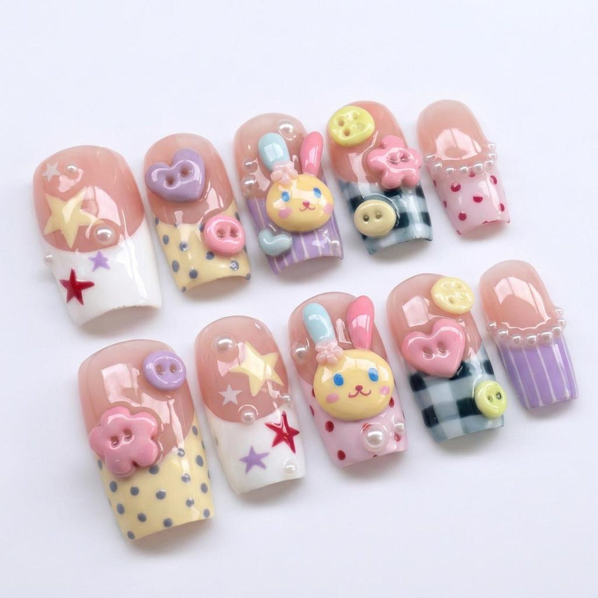 A set of ten artificial nails with a variety of designs. Each nail features a different design, including stars, hearts, bunnies, and buttons. The nails are painted in a variety of colors, including pink, yellow, and white. Some nails have a polka do