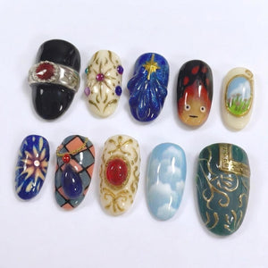 A collection of ten uniquely designed nail art pieces. The designs include a black nail with a ring, a cream-colored nail with gold accents, a blue nail with a star, a nail with a face, and a nail with a landscape. Other nails feature geometric patte