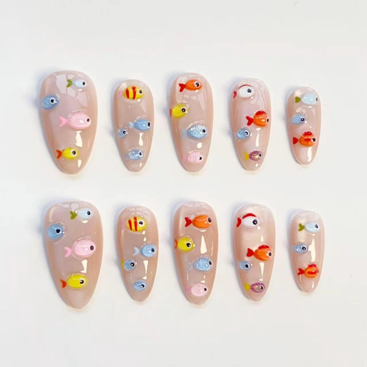 A set of ten artificial nails with a nude base color. Each nail is decorated with colorful, cartoon-style fish in shades of pink, yellow, orange, and blue. The fish have large, expressive eyes.