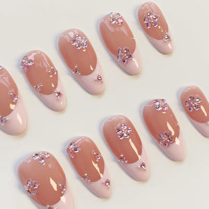 A set of artificial nails with a French manicure design. The nails feature a light pink base with a darker pink tip. Each nail is adorned with pink flower-shaped rhinestones and smaller accent gems.