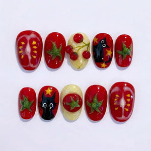 A set of ten artificial nails with a variety of designs. The nails feature red tomato slices, green tomato leaves, cherries, a black cat, and yellow stars. The nails are oval-shaped and have a glossy finish.