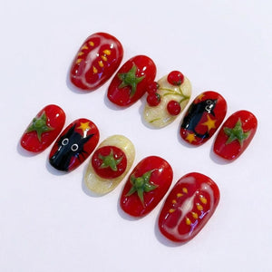A set of artificial nails with a tomato theme. The nails feature designs of red tomatoes, tomato slices, and green tomato leaves. Some nails have a black cat design with yellow stars.