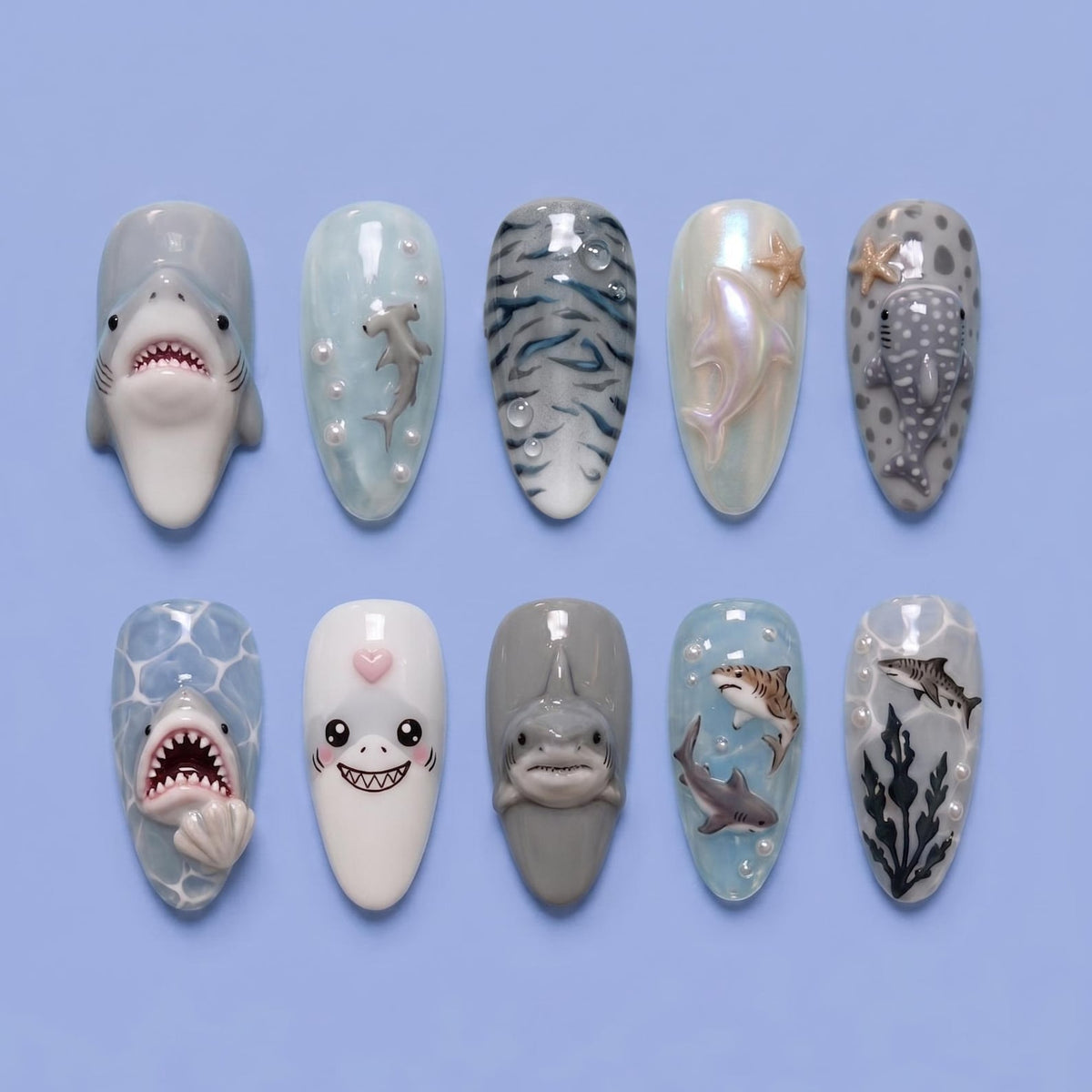 A collection of ten artificial nails with unique shark-themed designs. The nails feature various shark species, including hammerhead and whale sharks, with detailed 3D art and aquatic elements. The color palette includes shades of blue, gray, and whi