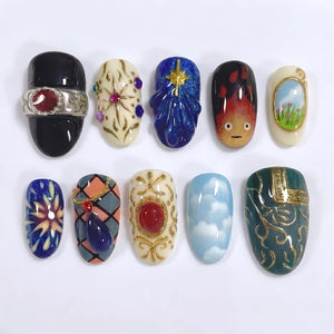 A collection of ten uniquely designed nail art creations. Each nail features intricate designs, including a black nail with a silver ring, a blue cloud design, and a nail with a landscape scene. The color palette includes blues, reds, golds, and crea
