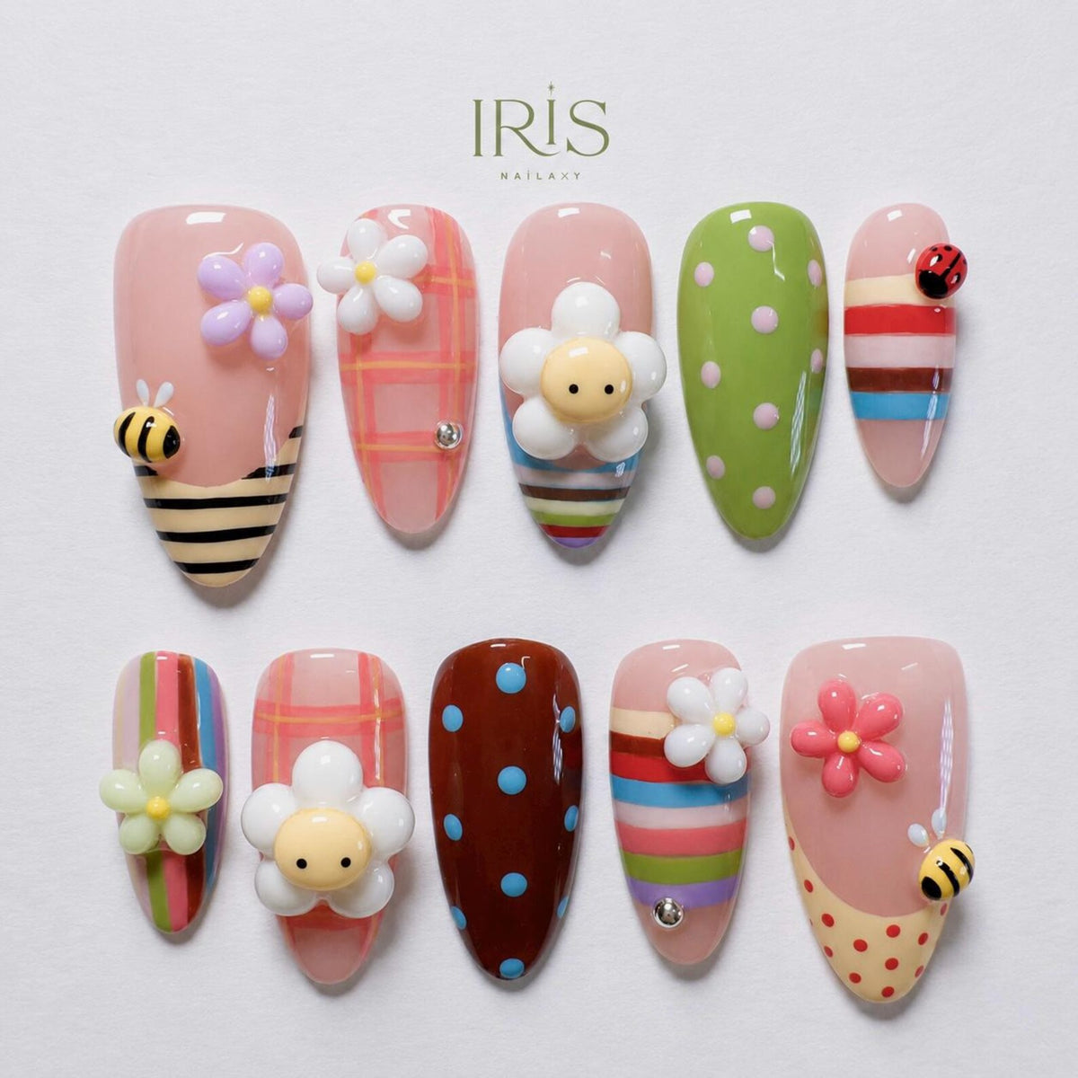 A set of ten artificial nails with various designs. The nails feature floral, bee, and ladybug embellishments, along with polka dots and striped patterns. The base colors include pink, green, and brown.