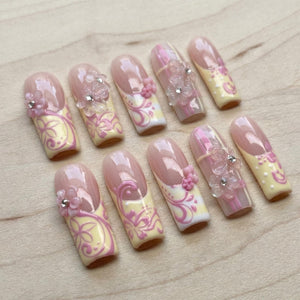 Set of ten artificial nails with a light pink and yellow design. Each nail features a floral embellishment and a decorative swirl pattern. The nails have a glossy finish.