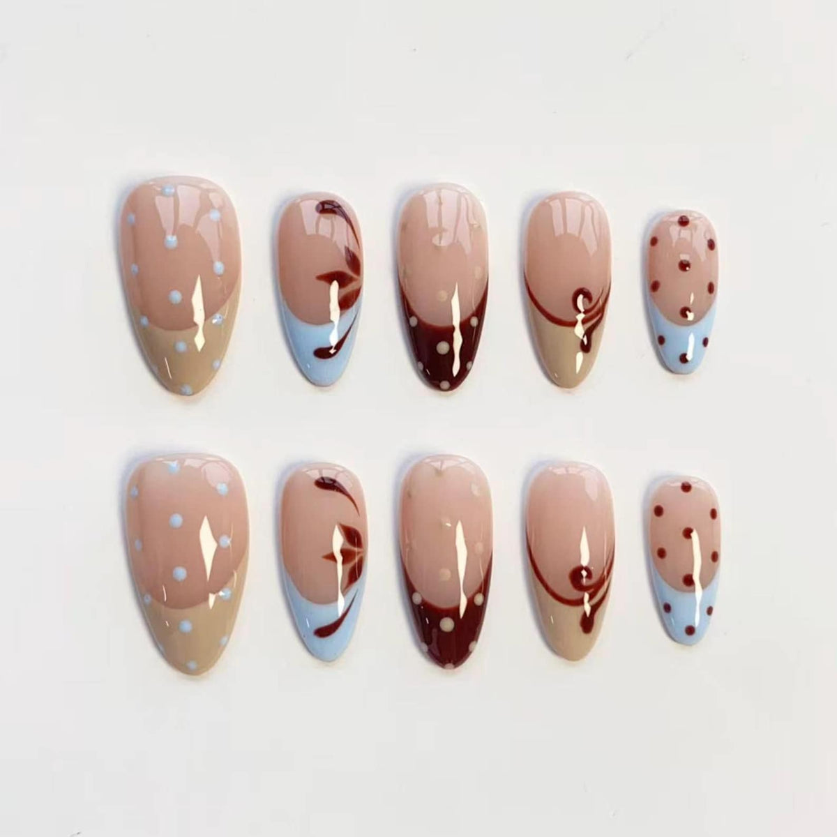 Set of ten almond-shaped false nails. The nails feature a variety of designs, including polka dots, floral patterns, and color-blocked sections in beige, burgundy, and light blue.