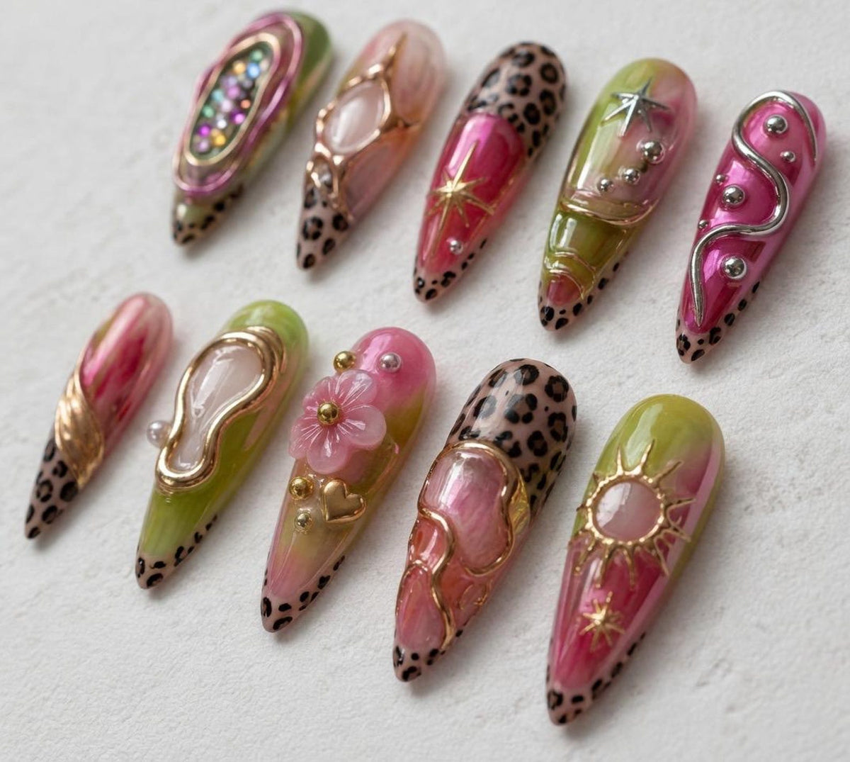 A set of ten almond-shaped press-on nails featuring a mix of pink and lime green gradients, leopard print tips, and 3D embellishments including gold metallic swirls, small pearls, a pink flower, a heart charm, and star accents.