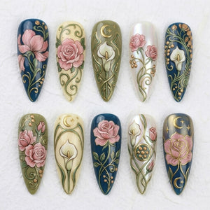 Ten almond-shaped artificial nail tips arranged in two rows. Each tip features intricate 3D-style relief designs of pink roses, white calla lilies, gold crescent moons, stars, and swirling green vines against dark blue, cream, and pearlescent backgro