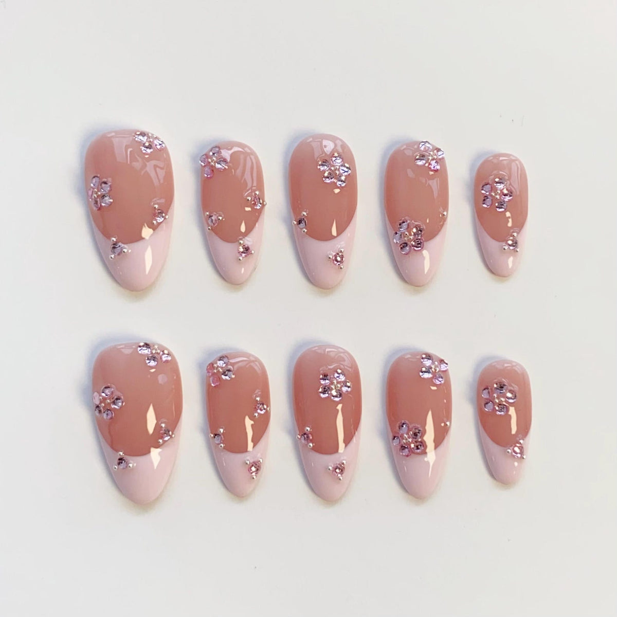 Set of ten oval-shaped false nails. Each nail features a light pink base with a darker pink tip. The nails are adorned with small, pink flower-shaped rhinestones. The design is consistent across all nails.