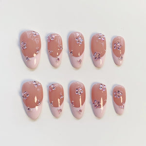 Set of ten oval-shaped false nails. Each nail features a light pink base with a darker pink tip. The nails are adorned with small, pink flower-shaped rhinestones. The design is consistent across all nails.