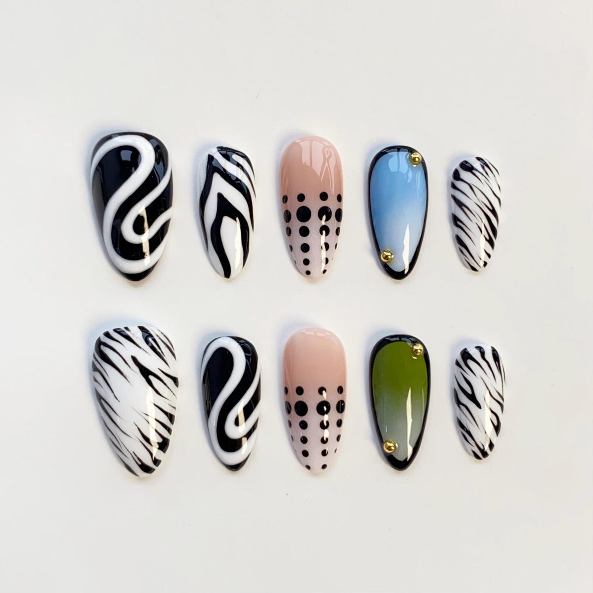 A set of ten artificial nails in various designs. The nails feature patterns like black and white swirls, zebra stripes, and dotted designs. Some nails have a gradient of color, and some have small gold accents.