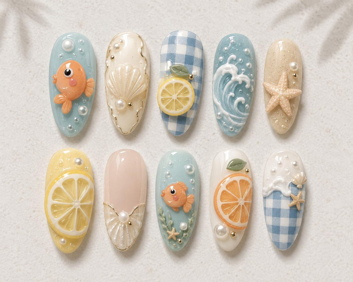 A set of ten press-on nails featuring 3D designs including orange goldfish, white seashells, yellow and orange citrus slices, blue and white gingham patterns, ocean waves, starfish, and small white pearls on various pastel backgrounds.