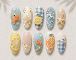 A set of ten press-on nails featuring 3D designs including orange goldfish, white seashells, yellow and orange citrus slices, blue and white gingham patterns, ocean waves, starfish, and small white pearls on various pastel backgrounds.