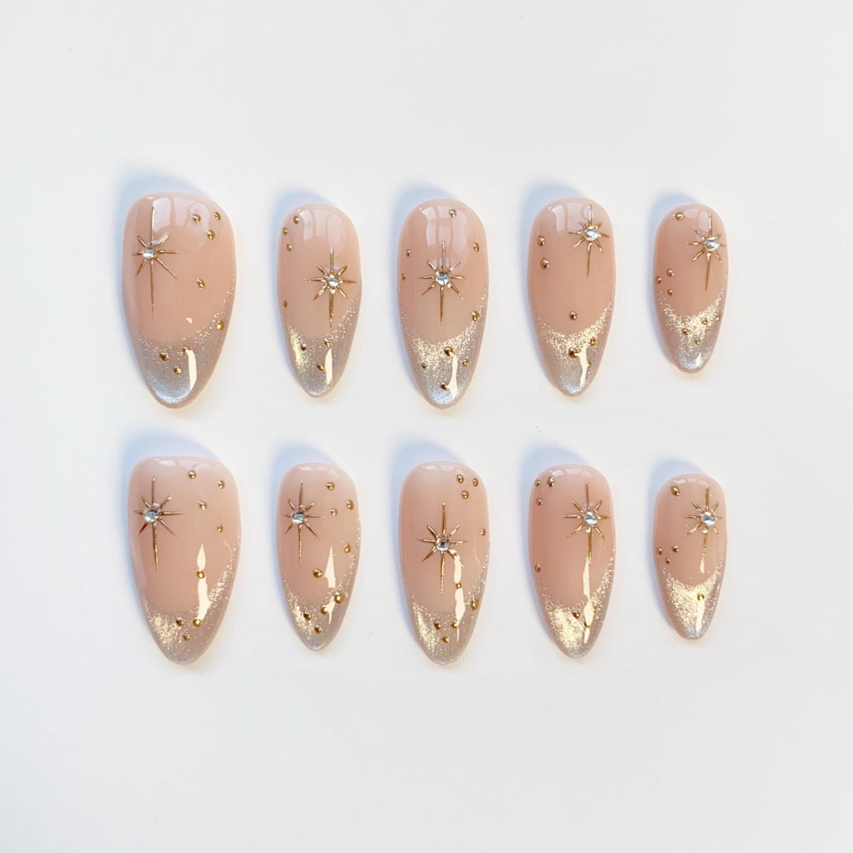 Set of ten almond-shaped false nails. Each nail is painted a light pink with a silver glitter gradient at the tip. Gold star and dot accents are featured on each nail, with a central rhinestone star.