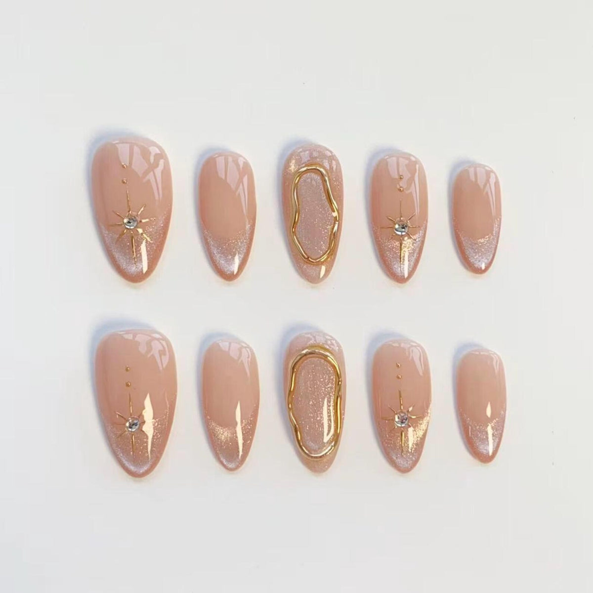 A set of ten almond-shaped press-on nails in a nude base color. The design features gold starburst accents with small embedded crystals, silver glitter tips, and a raised gold metallic organic oval frame on the middle fingernails.