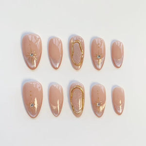 A set of ten almond-shaped press-on nails featuring a nude base with silver glitter tips. The design includes gold starburst accents with small clear rhinestones and raised gold metallic organic oval frames on the center nails.