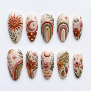 A set of ten almond-shaped press-on nails featuring a cream base with raised 3D designs. The patterns include a sun face, crescent moons, rainbows, stars, and various floral and botanical elements in shades of terracotta, sage, and pink.