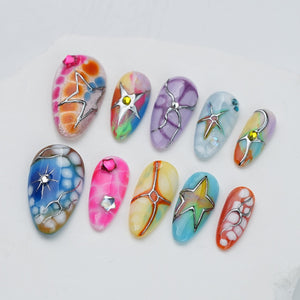 A set of ten press-on nails featuring various colorful marbled patterns, metallic silver star-shaped accents, and small embedded rhinestones. Each nail has a unique design with vibrant hues including pink, blue, orange, and purple.