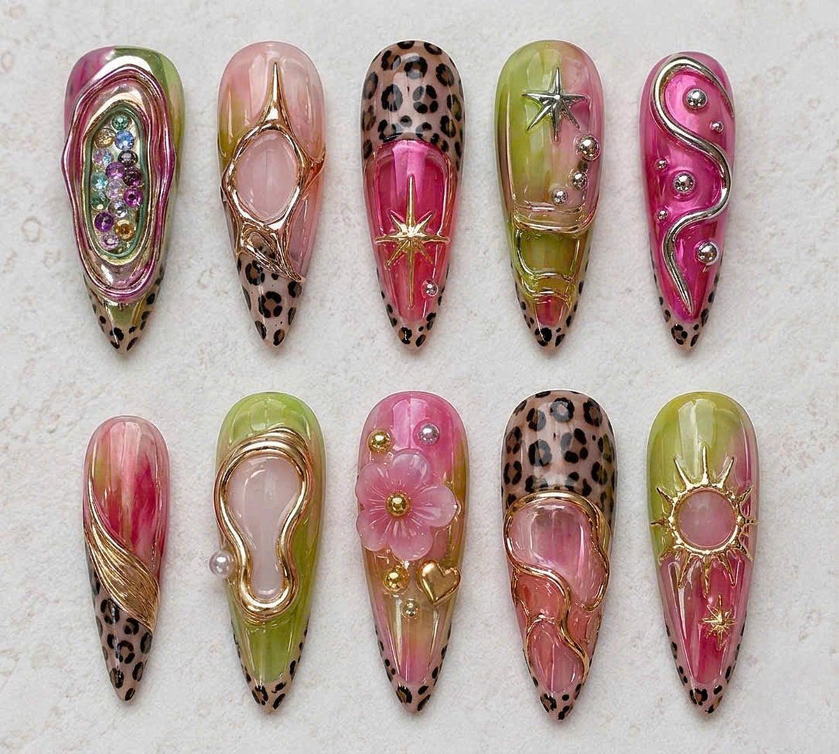 A set of ten almond-shaped press-on nails featuring a mix of pink and lime green marbled bases, leopard print tips, and 3D metallic gold and silver accents including stars, flowers, hearts, and small rhinestones in various colors.