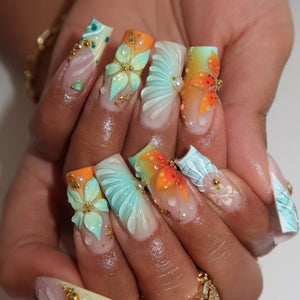Square-shaped artificial nails featuring a gradient of orange and mint green. The design includes three-dimensional sculpted flowers, ribbed shell-like textures, small gold metallic beads, and clear droplet accents over a nude base.