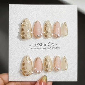 A set of ten press-on nails arranged in two rows on a white display card labeled LeStar Co - LITTLE LUXURIES FOR YOUR NAIL TIPS. The nails feature a mix of cream and soft pink tones with gold leaf flo