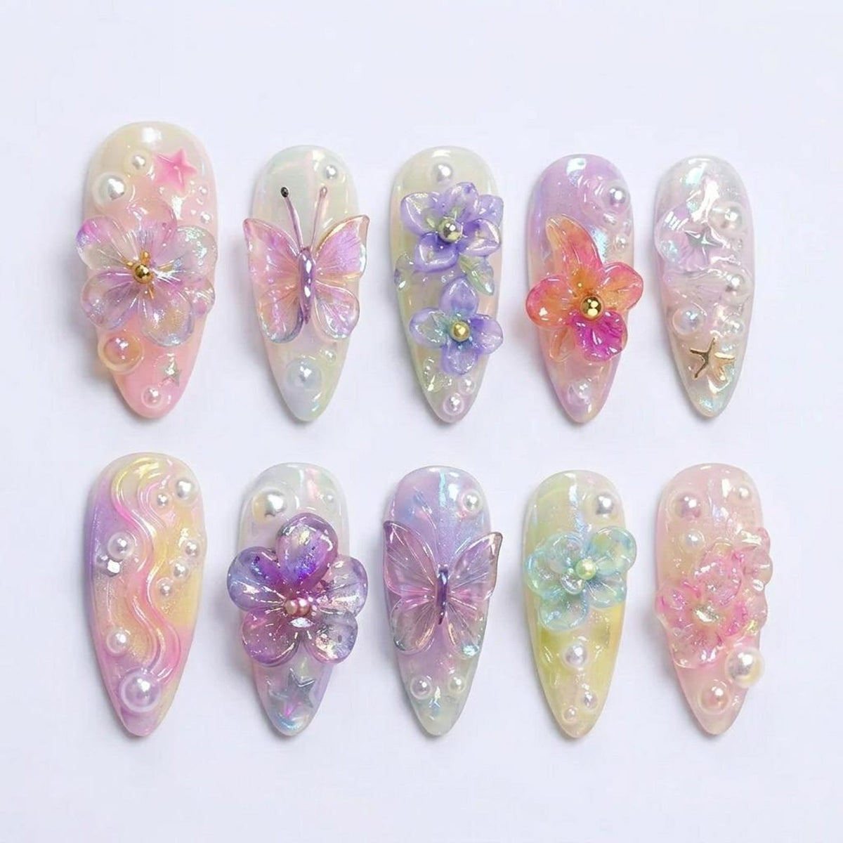 A set of ten almond-shaped press-on nails featuring a pastel iridescent finish. The designs include three-dimensional acrylic butterflies, purple and pink floral accents, small white pearls, and tiny gold star charms arranged on each nail.