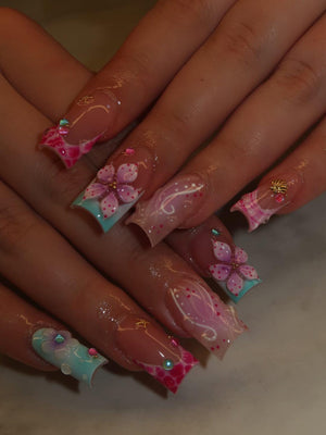 Long square-shaped artificial nails featuring a French manicure base with a gradient of pink and light blue. The design includes three-dimensional pink floral accents, white swirl patterns, small pink dots, and tiny gold and blue embellishments.