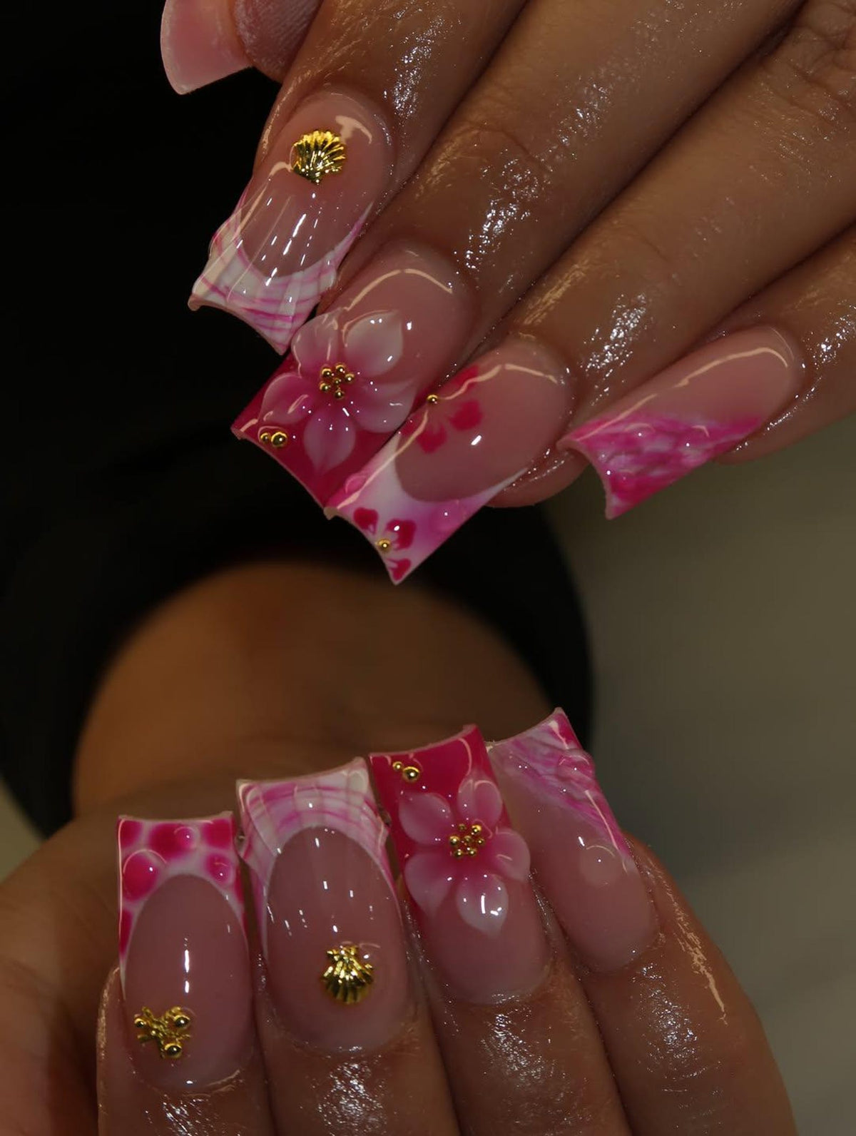 Long square-shaped artificial nails featuring a nude base with pink and white marbled tips. The design includes three-dimensional white floral accents with gold centers, small gold shell-shaped charms, and gold bead embellishments.
