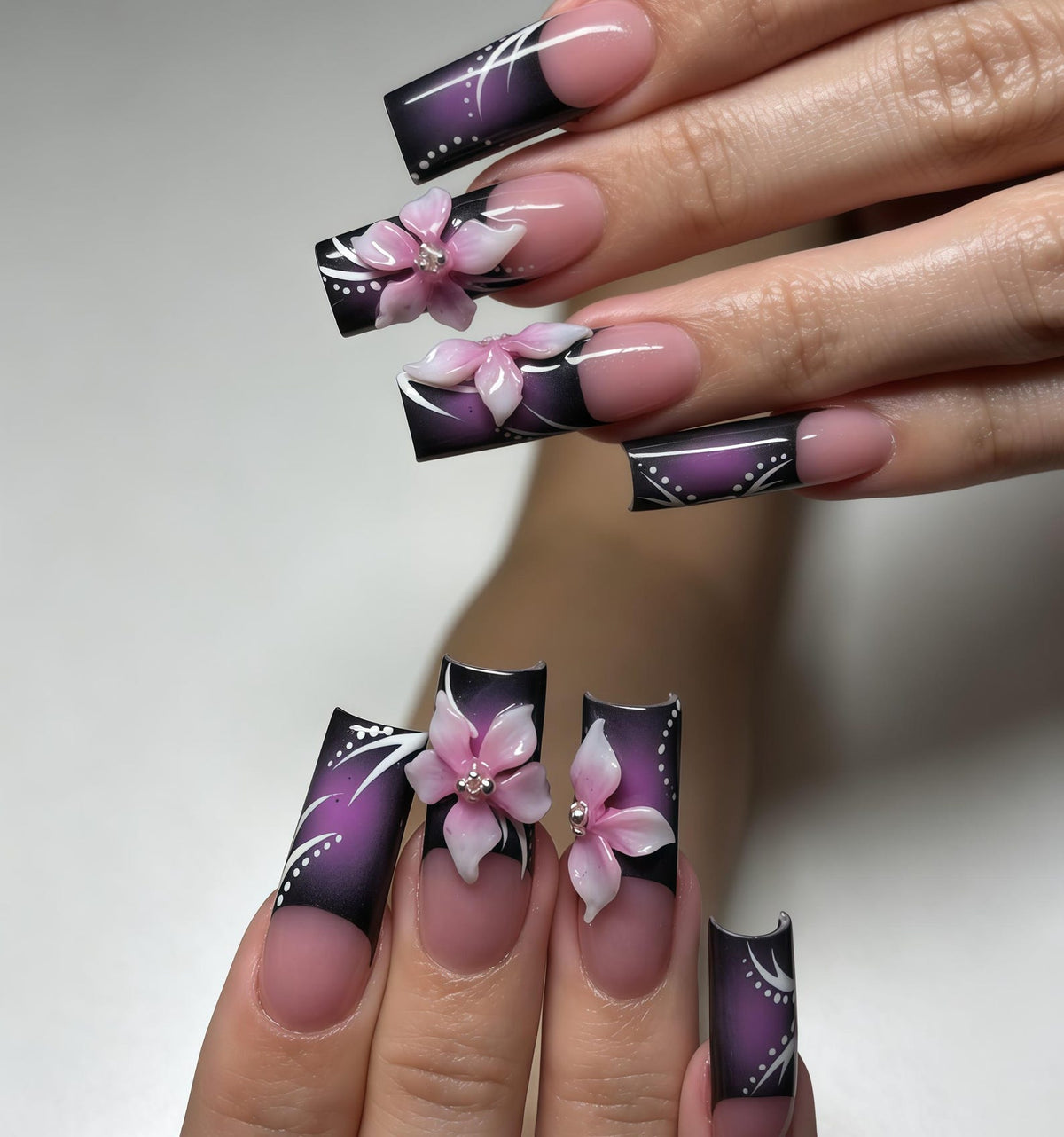 Long square-shaped artificial nails featuring a dark purple and black gradient French tip design. The nails are decorated with white painted swirls, small white dots, and three-dimensional pink floral accents with a central crystal.