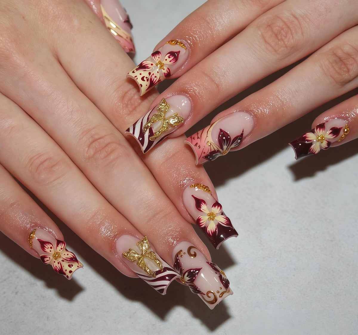 Long square-shaped artificial nails featuring a nude base with deep burgundy floral patterns, gold metallic butterfly accents, and intricate gold swirl detailing. The design incorporates small gold beads and white highlights.