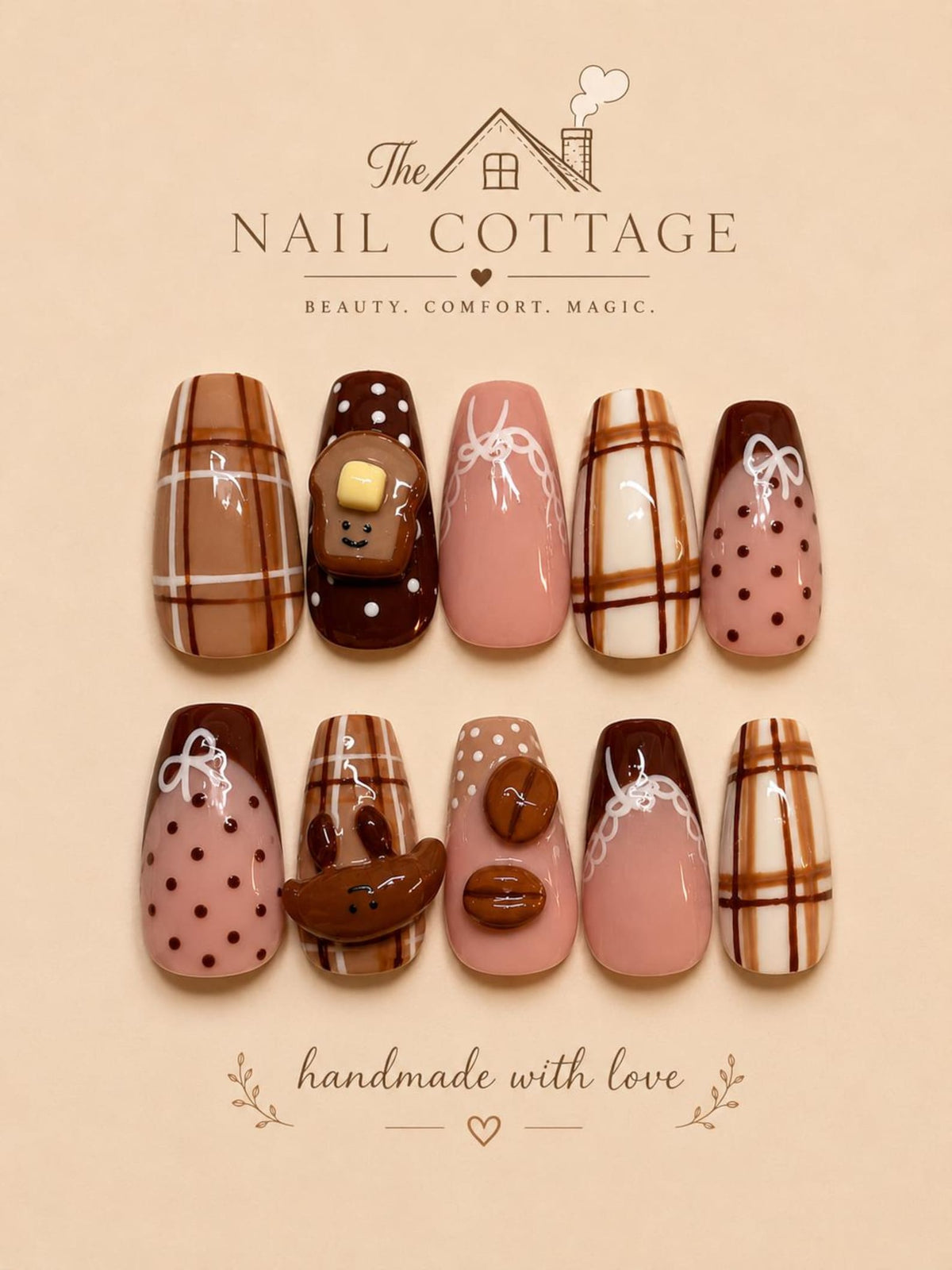 A set of ten press-on nails featuring brown, cream, and pink tones with plaid patterns, polka dots, and 3D charms including a smiling toast, coffee beans, and a bear face. The text reads The NAIL COTTAGE BEAUTY. COMFORT. MAGIC. handmade with love.