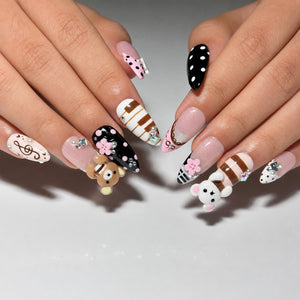 Ten pink, black, brown and white almond press on nails with 3D teddy bear charms, flowers, music notes, polka dots, stripes, pearls and rhinestones on a white background.