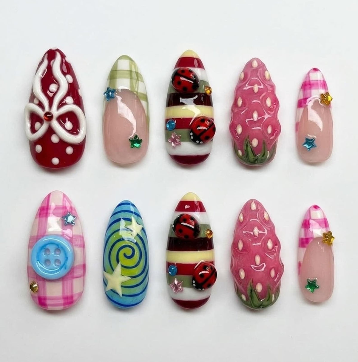 A set of ten almond-shaped press-on nails featuring diverse designs including red polka dots with a white bow, green and pink plaid, ladybugs on striped backgrounds, pink textured strawberry patterns, blue swirls, and a light blue button.