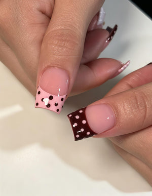 Square-shaped artificial nails featuring a French manicure style with a glossy finish. One nail has a light pink tip with dark brown polka dots, while the other has a dark brown tip with light pink polka dots over a nude base.
