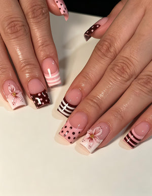 Square-shaped fingernails featuring a French manicure style with a nude base. The tips are decorated with alternating patterns including dark brown and light pink horizontal stripes, dark brown with white polka dots, and hand-painted pink flowers wit