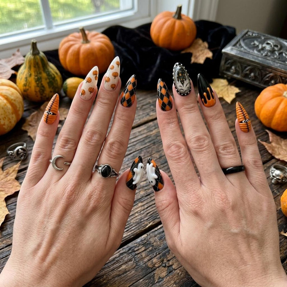 Stiletto-shaped press-on nails featuring a variety of Halloween-themed designs including orange pumpkins, black and orange argyle patterns, white ghosts, black drip art, and a central haunted house graphic on a dark, textured background.