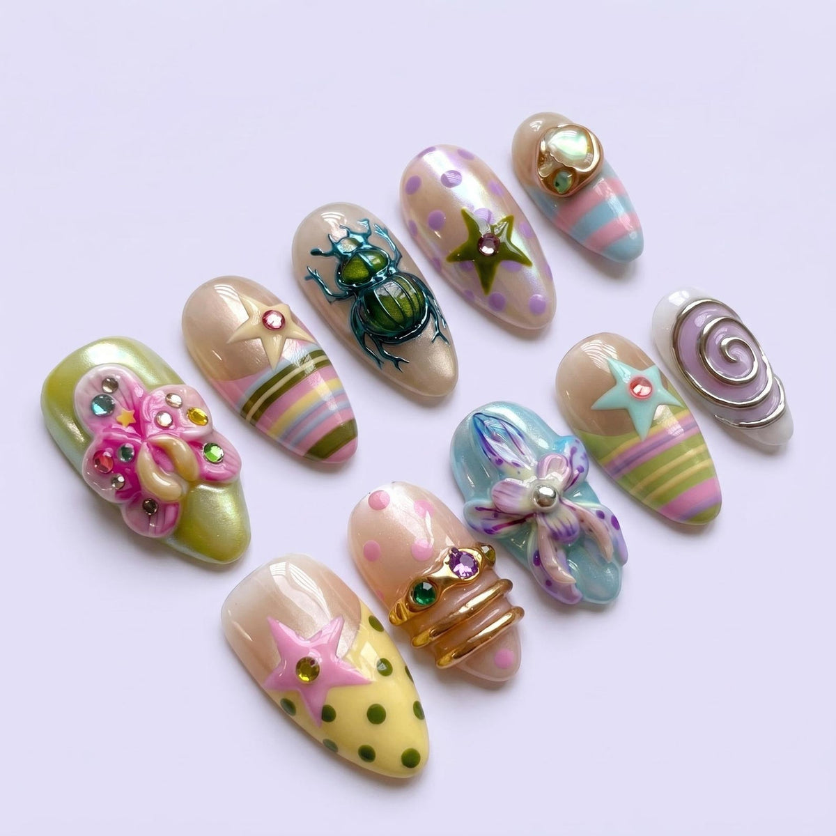 A collection of ten almond-shaped press-on nails featuring diverse designs including a metallic green beetle, pastel polka dots, striped patterns, 3D floral embellishments, star motifs with rhinestones, and gold-toned metal accents.