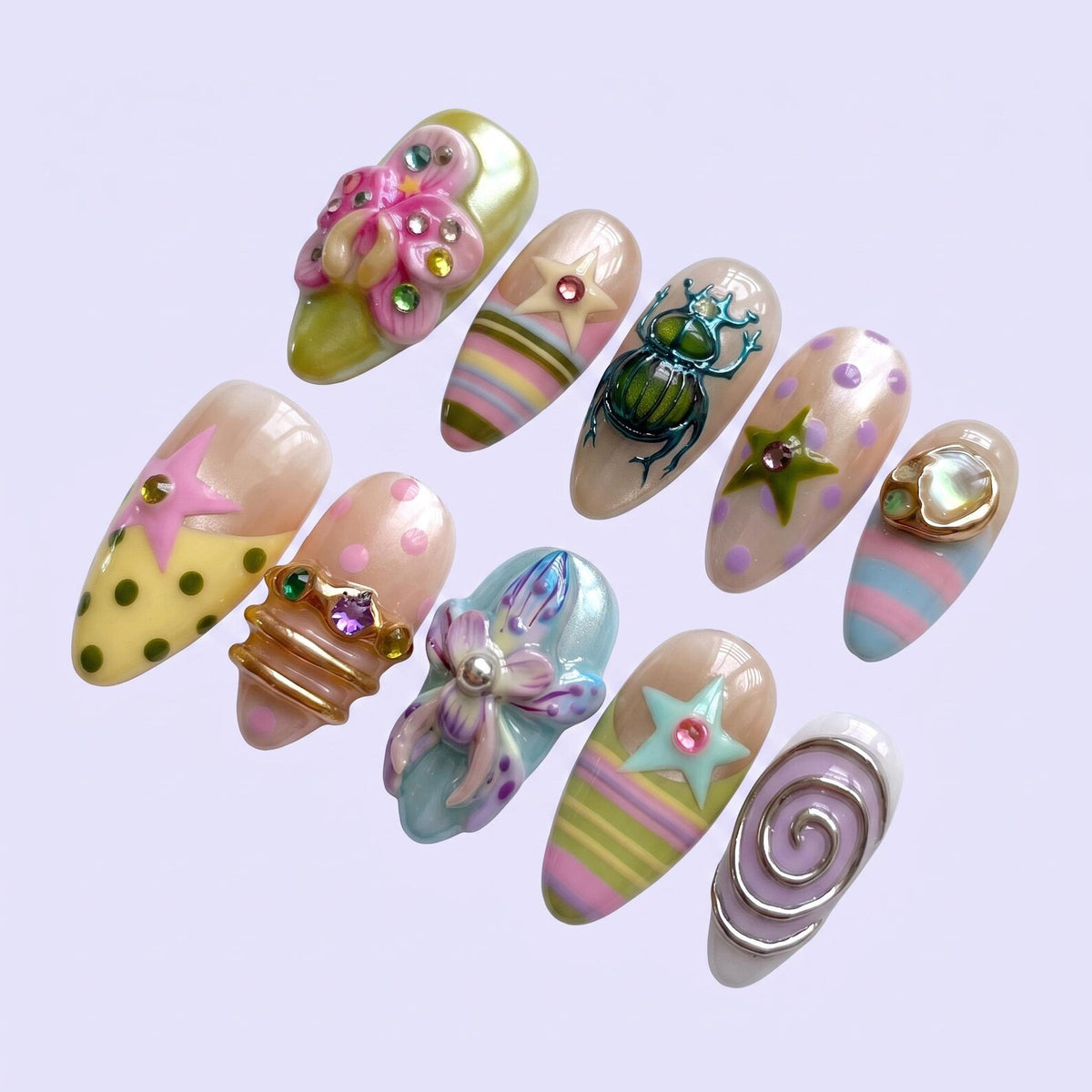 A set of ten almond-shaped press-on nails featuring diverse designs including 3D floral embellishments, a metallic beetle, pastel stripes, polka dots, stars with embedded rhinestones, gold-toned rings, and a silver-toned spiral accent.