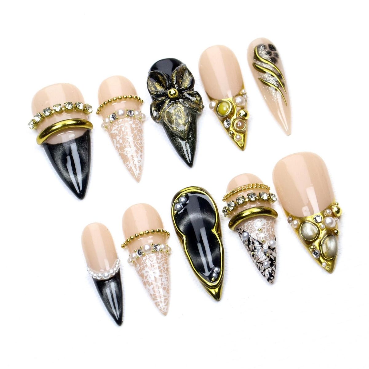 A set of ten stiletto-shaped press-on nails featuring a nude base with black tips, white lace patterns, gold metallic accents, and embedded rhinestones and pearls. The designs include solid black, lace-covered, and jeweled embellishments.