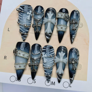 A set of ten press-on nails featuring a dark blue and black gradient base with white zebra-like stripes, silver metallic chains, small silver studs, and three-dimensional white and silver cross charms arranged on a display card.