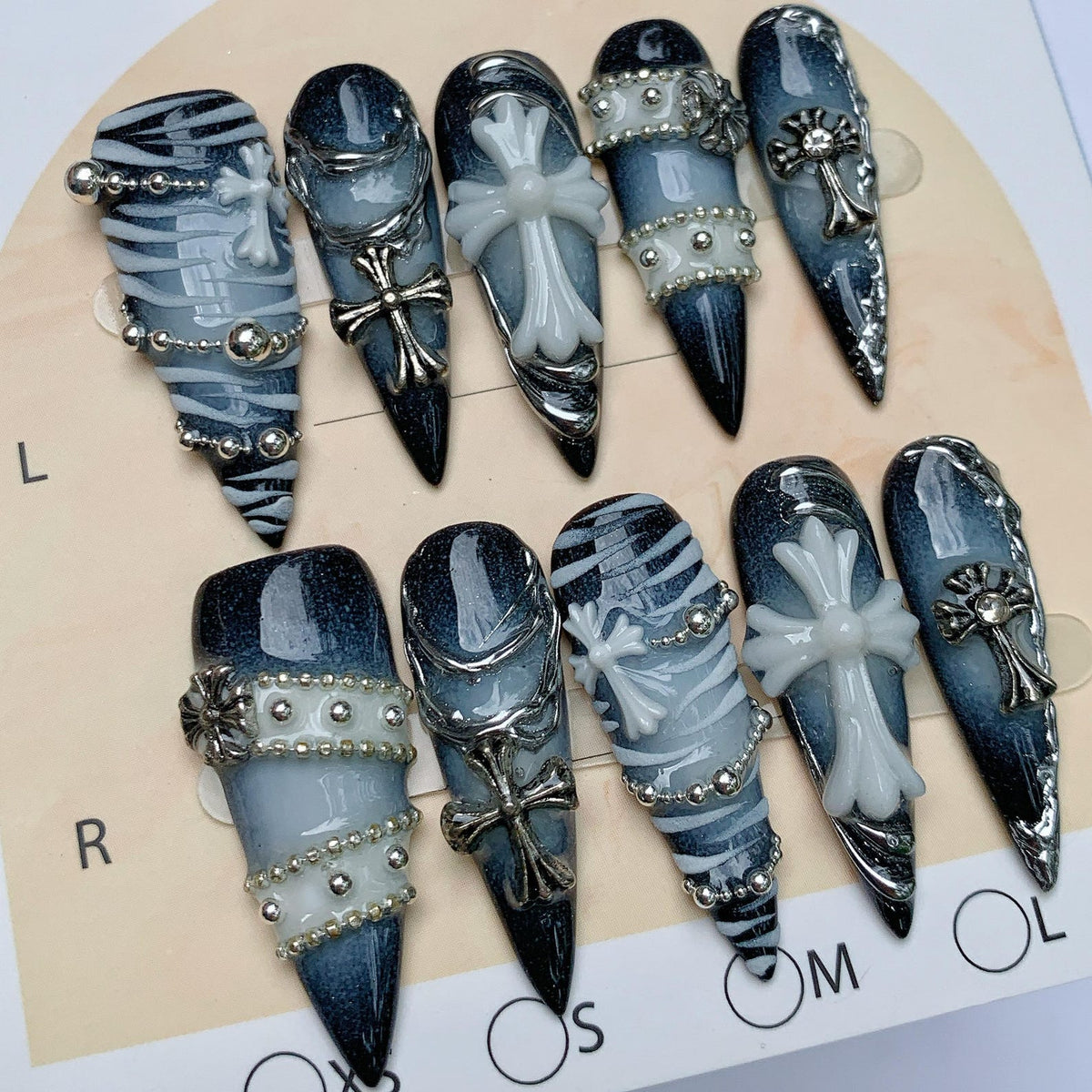 A set of ten stiletto-shaped press-on nails featuring a dark blue and black gradient base. The designs include white zebra-like stripes, silver metallic chains, small silver studs, and raised white or silver cross emblems.