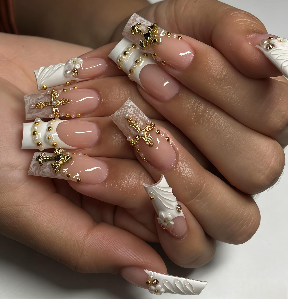 Long square-shaped artificial nails featuring a French manicure base with white lace-patterned tips. The nails are decorated with gold-toned cross charms, small white floral accents, and tiny gold and white spherical beads.