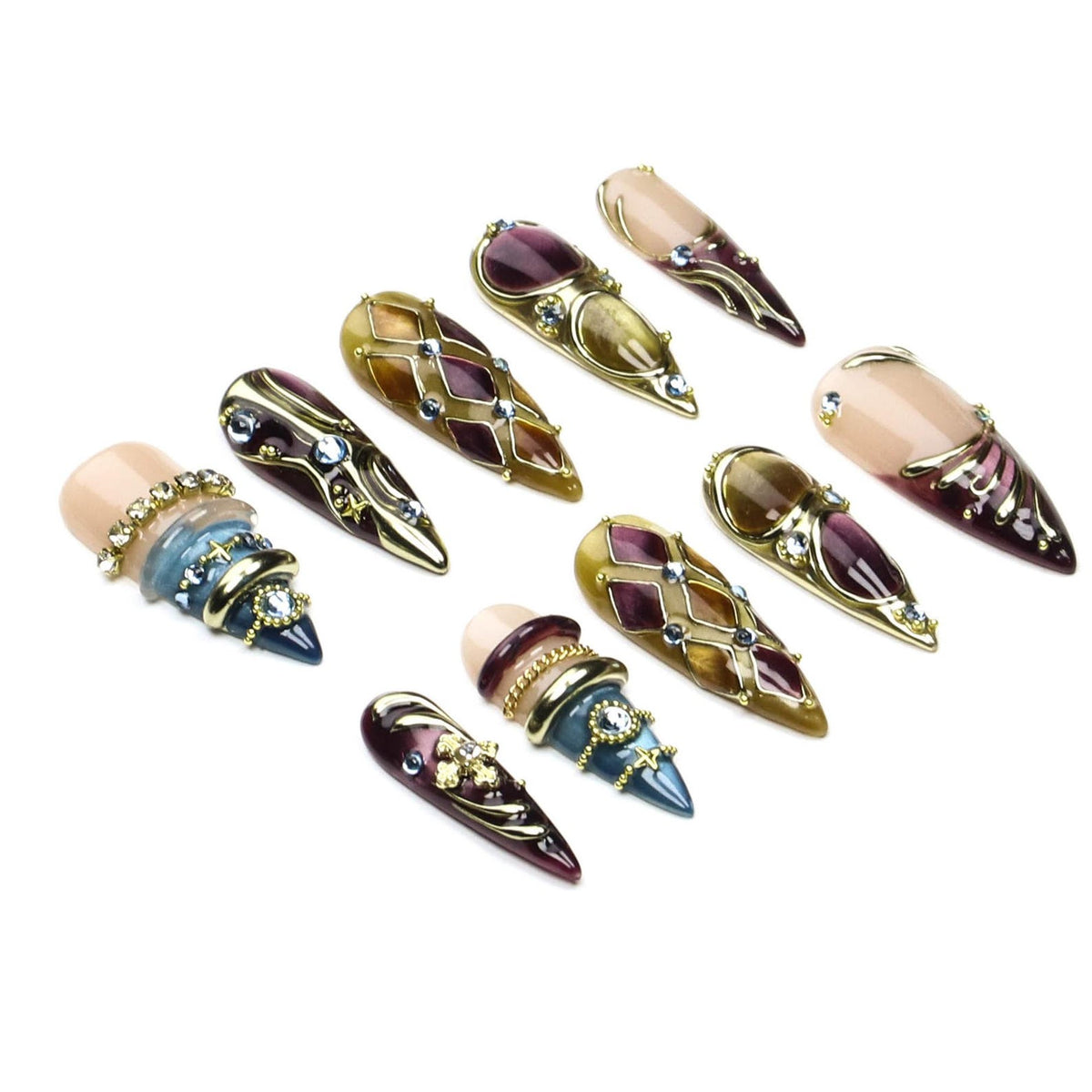 A set of ten stiletto-shaped press-on nails featuring a variety of designs including deep purple and gold lattice patterns, metallic accents, embedded rhinestones, and smooth nude-toned bases with ornate gold-toned embellishments.