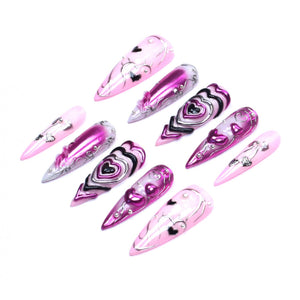 A set of ten stiletto-shaped press-on nails featuring a color palette of light pink, magenta, and black. The designs include metallic silver accents, raised heart motifs, and intricate line work, with some nails displaying a glossy finish.